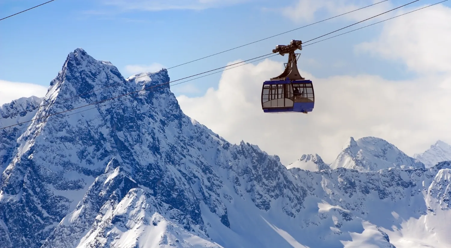 Seilbahn vor verschneiten Alpengipfeln